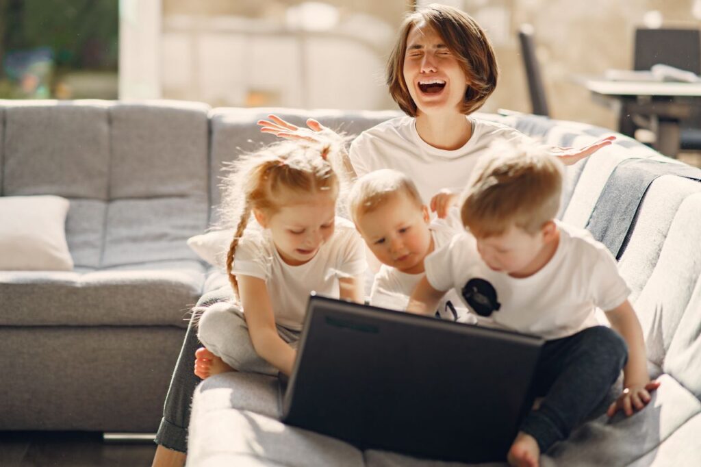 Stressed woman asking for help while sitting with small children playing on laptop together on sofa in living room